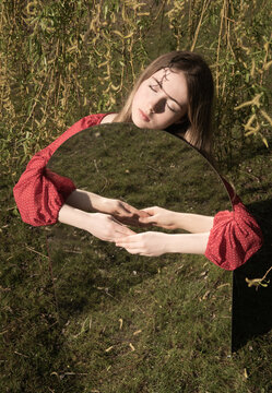 fine art portrait of girl in red dress embracing large mirror in field in spring