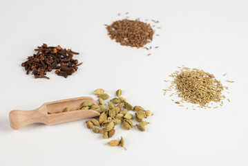 cardamom in a wooden spoon with other spices on a white background