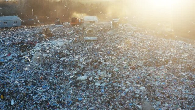 Aerial view of a city dump. A flock of birds is circling over the garbage dump. Garbage trucks unload garbage. Bulldozers crush rubbish and waste