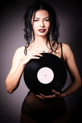 Vintage photo of a glamorous pinup girl, holding a vinyl record and looking up on a pink background.