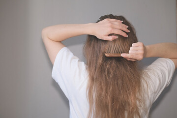 Woman combing her tangled blond hair in a white t-shirt on a gray background.  Tangled hair. Combing hair