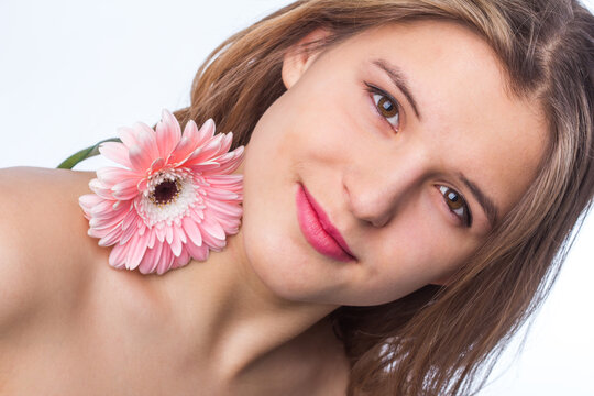 Portrait of a happy girl with fresh skin holding a flower over one eye on white background. Close up portrait of beautiful redhead curly woman pnik flower wearing white tshirt. Beauty and spring