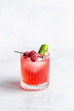 Raspberry and lime cocktail with frozen raspberries and lime garnish.