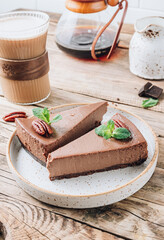 Chocolate cheesecake with pecans and mint, coffee cup on rustic wooden background.