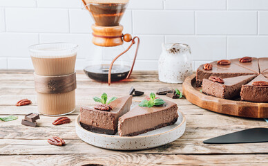 Chocolate cheesecake with pecans and mint, coffee cup on rustic wooden background.