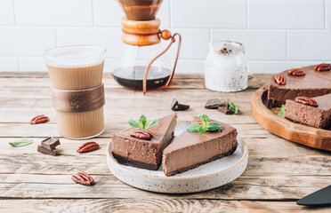 Chocolate cheesecake with pecans and mint, coffee cup on rustic wooden background.