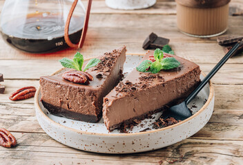 Chocolate cheesecake with pecans and mint, coffee cup on rustic wooden background.