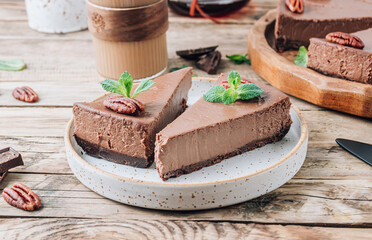 Chocolate cheesecake with pecans and mint, coffee cup on rustic wooden background.