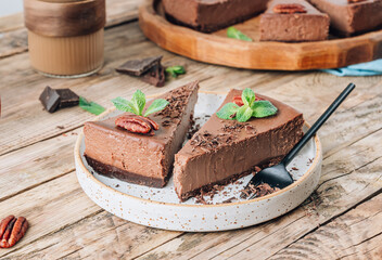 Chocolate cheesecake with pecans and mint, coffee cup on rustic wooden background.