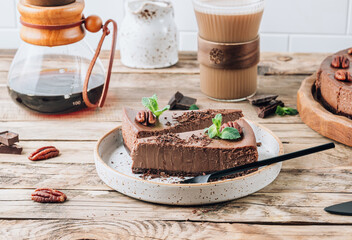 Chocolate cheesecake with pecans and mint, coffee cup on rustic wooden background.