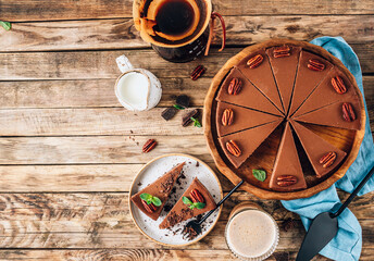 Chocolate cheesecake with pecans and mint, coffee cup on rustic wooden background.