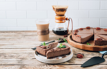 Chocolate cheesecake with pecans and mint, coffee cup on rustic wooden background.