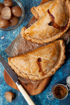 Several Cornish pasties on a wooden board served with pickled onions.