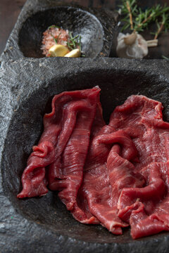 Raw beef fillet on black stone plate and mortar with herbs. Black background