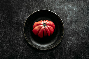 raw beef heart tomato, placed on a black plate, on a black textured background. view from above