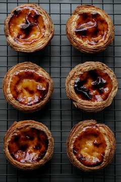 Six Pasteis de nata (small traditional Portuguese cake) placed on a pastry grid on a dark gray background. Top view