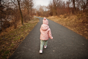 Back of running baby girl in pink jacket on the path.