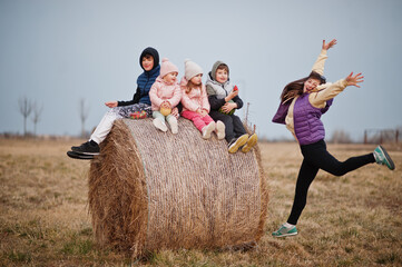 Four kids with mother having fun on haycock at field.