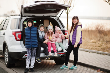 Mother with four kids sitting in trunk of big suv car. - obrazy, fototapety, plakaty