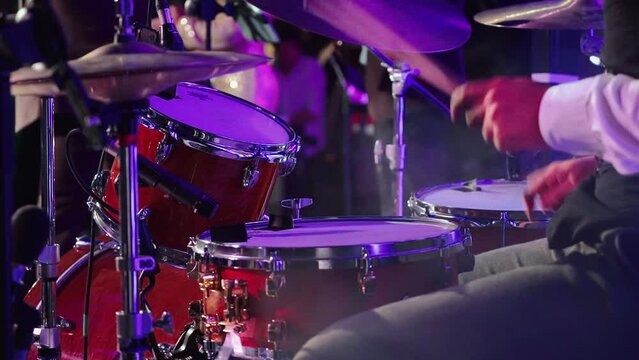 Man plays drums in evening and musicians sing on stage.
