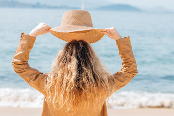 woman with hat on the beach looking at the sea