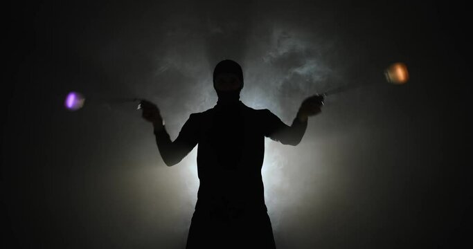 Man in balaclava mask spinning led poi hand props in illuminated background with smoke