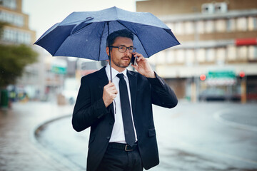 Ill be in the office soon. Shot of a mature businessman talking on a cellphone and holding an umbrella while out in the city.