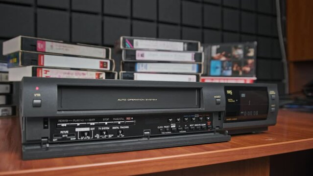 Eject VHS tape cassette from VCR player. Man pulls out VHS from vintage videotape recorder with counter on desk with many video cassettes. VHS retro player. Concept home video, archive, old Technology