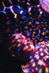 Vertical shot of a baby boy looking at his star projector lamp covered with colorful light stars....