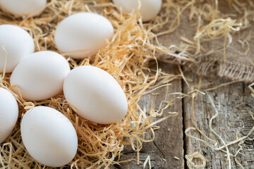 White chicken eggs on the straw or hay on burlap cloth and wooden boards
