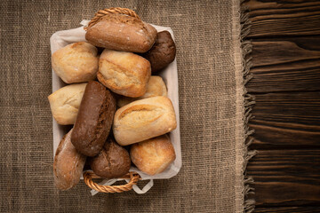 Wheat and rye bread in a wicker basket on a burlap cloth on a brown wooden table