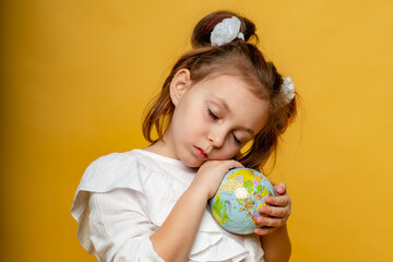 a cute six-year-old girl with her eyes closed hugs a mock-up of the Earth