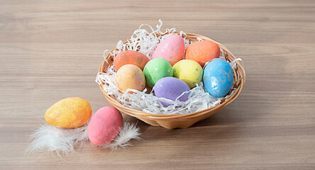Easter colorful eggs in a wicker basket on a wooden brown table. Krypny plan. Soft focus.