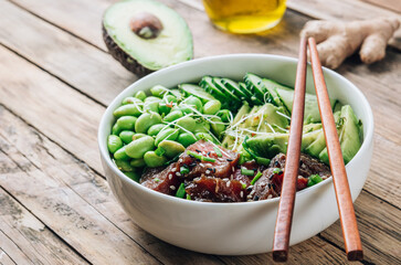 Poke bowl with raw tuna, rice, avocado, edamame beans and cucumber in a bowl. Hawaiian ahi poke bowl