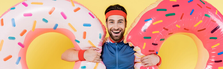 Cheerful sportsman holding swim rings isolated on yellow, banner.