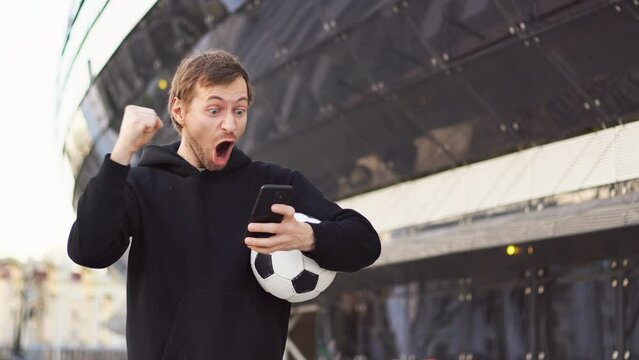 Man celebrate win a bet with a soccer mobile app. football bet, sports gambling. Football stadium on the background. Copy space.