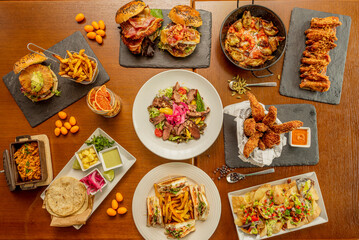 Set of homemade fast food dishes, sandwiches, Mexican al pastor tacos, burgers with fruits, quesadillas and nachos, barbecue wings, chicken fingers and salad with duck confit