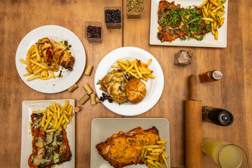 Argentinian food plate with a hamburger and several milanesas of different conception, French fries, arugula, pepper and bell pepper, a wooden rolling pin and various types of spices