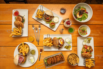 Plate set with assorted burgers, goat cheese salad, nachos, pickles, french fries, chicken medallions, assorted sauces, guacamole