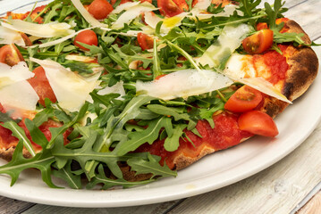 Detail of a delicious pizza, with Parmesan cheese shavings, arugula in abundance, pomodoro sauce and chopped cherry tomatoes with Spanish olive oil