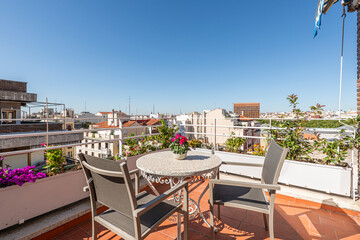 Nice terrace in a penthouse apartment with lots of flowers, a round stone table and matching chairs with views of the city