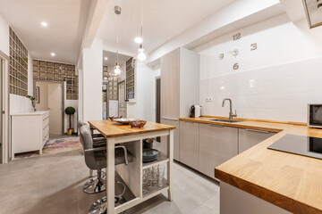 Kitchen with gray cabinets and solid pine countertops, glass paved walls in back and matching island with chrome metal and gray leather chairs