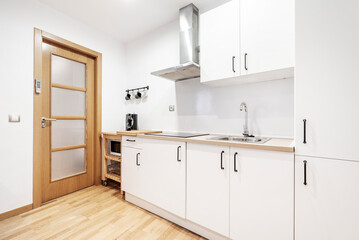 Kitchen with white cabinets and light wood countertops with matching wood cabinets, stainless steel range hood, light wood flooring and glass door