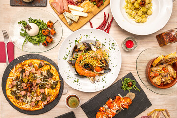 Top view of Italian food dishes, with pizza with sausages, pasta with shrimp marinara, burrata salad, antipasto plate, gnocchi with tomato, oils, peppers