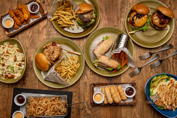 Set of fast food dishes with assorted hamburgers, sandwiches, sweet potato fries, tequeños, fried chicken strips and caesar salad