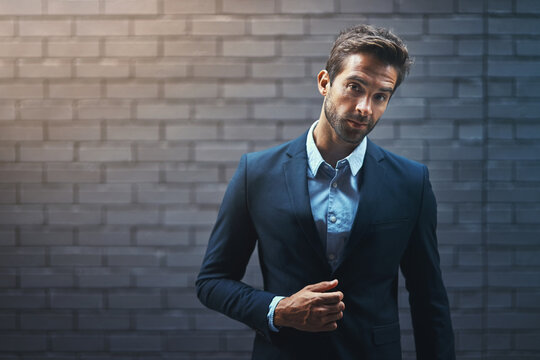 Dress for success and then go out and get it. Portrait of a handsome young businessman standing against a grey facebrick wall.