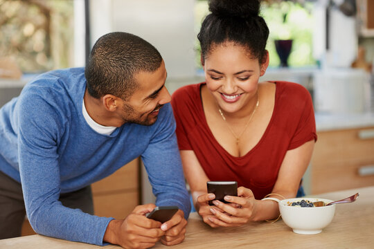 Making smart technology work in their marriage. Shot of a happy young couple using their smartphones together at home.