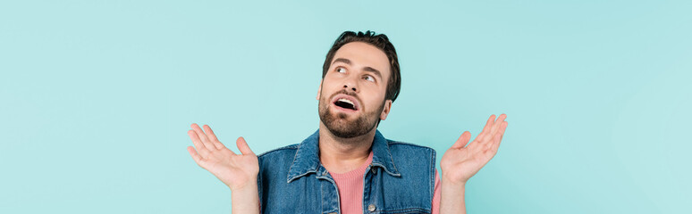 Fototapeta premium Young shocked man looking away isolated on blue, banner.