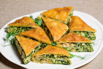 Salmon with spinach and herbs, baked in puff pastry, served with green dill on a plate. Homemade delicious pie. traditional fish dish