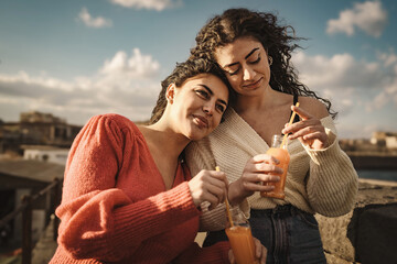 Two brunette teen friends enjoy a weekend outdoors drinking orange juice from the bottle with...